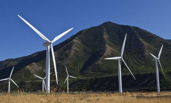 White wind turbines against backdrop of green, tree covered mountains and blue sky