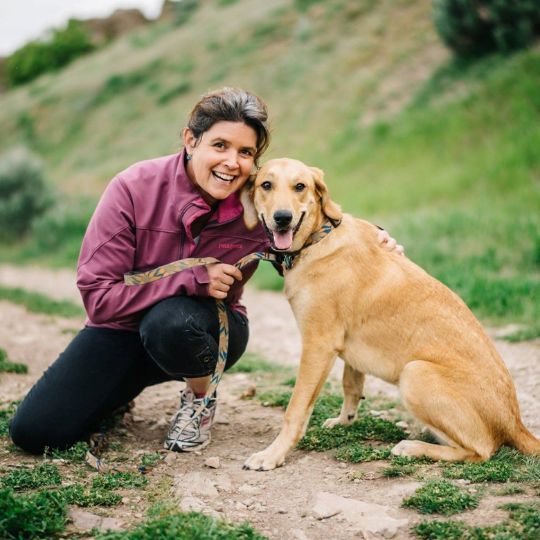 A women smiling with a dog on a trail.