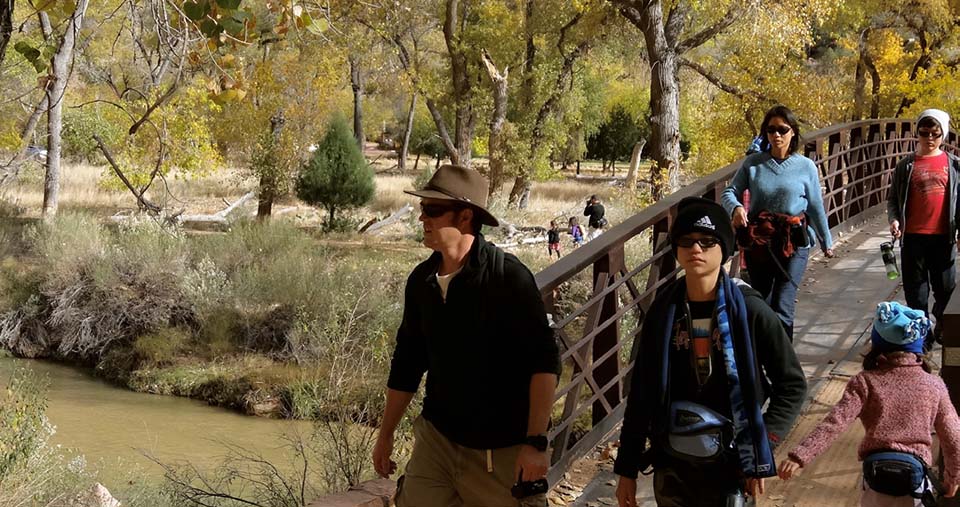 Park visitors crossing a bridge over a stream with fall foliage in background