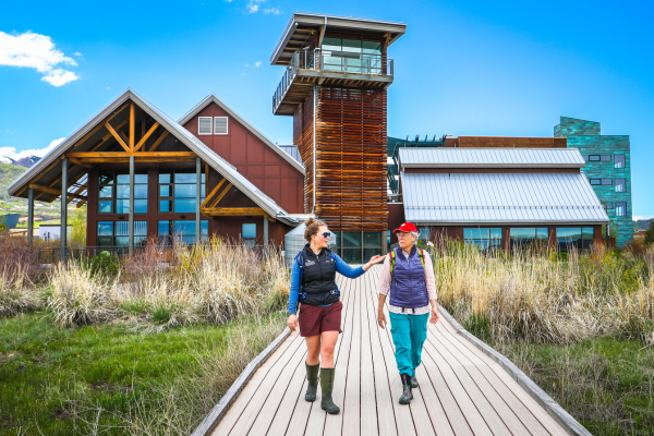 Two people walking down boardwalk with the EcoCenter in the background