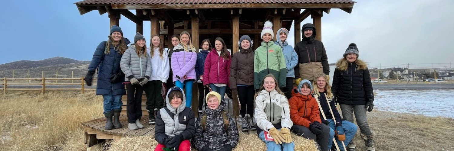 Group of teenagers and some adults posing in front of a wooden pavillion on a nature preserve; it's cold outside so they're all bundled up in coats and beanies.