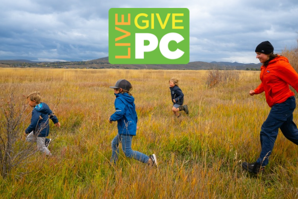 Adult and three kids running through golden grasses on a nature preserve; overlaid above them is a green and orange logo reading, "Live PC Give PC"