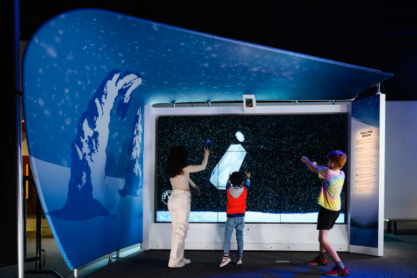 three children interacting with large touch screen with snow crystals on it