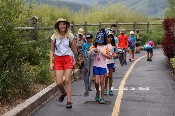 adult leading children down a bike path in the summer with mountains in the background