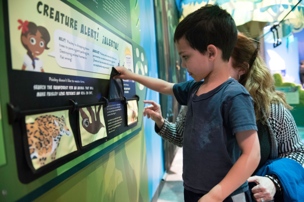 Child and adult lifting a panel up on an educational Wild Kratts-themed exhibit.