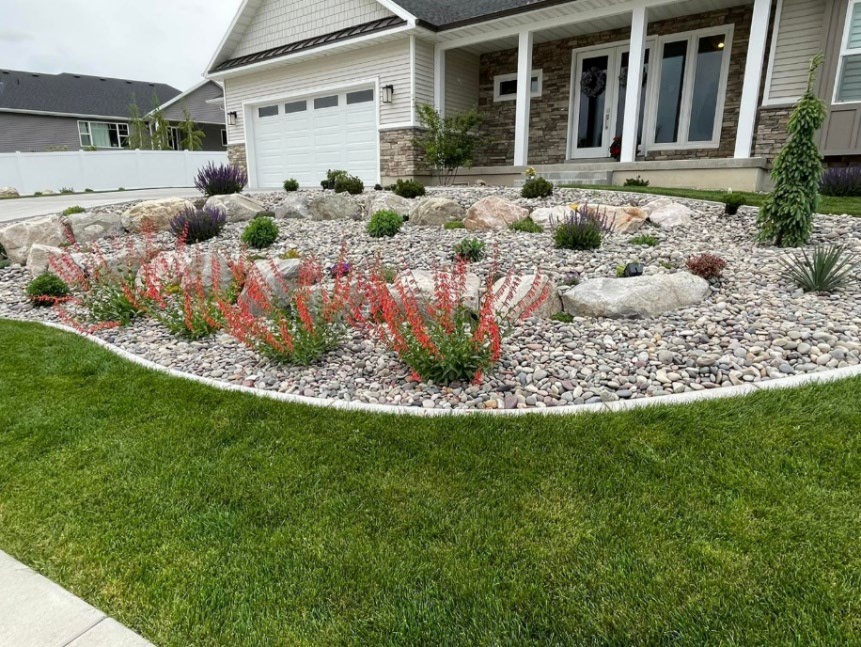 A home with agravel flowerbed within the front yard with flowers and other plants