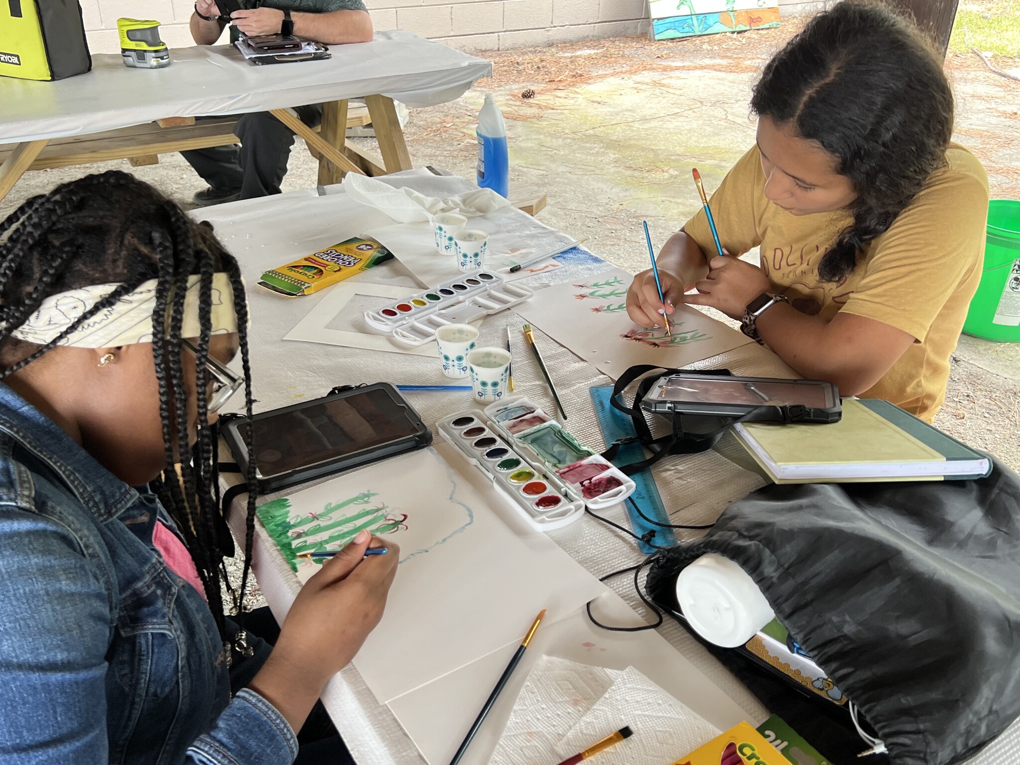 Two girls using watercolor to paint flowers from microscope photographs.