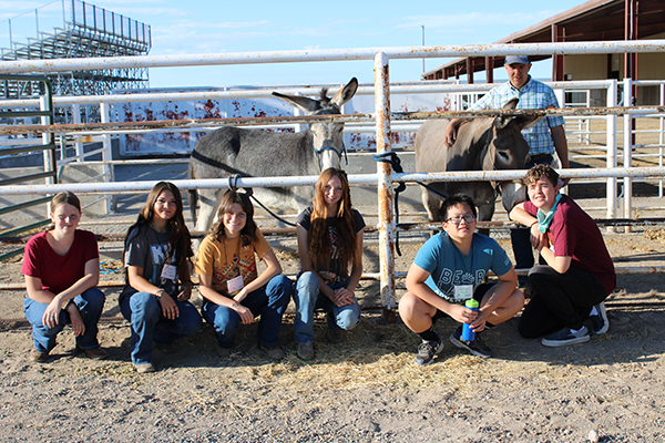 Group of youth posing in front of burro standing behind a gate