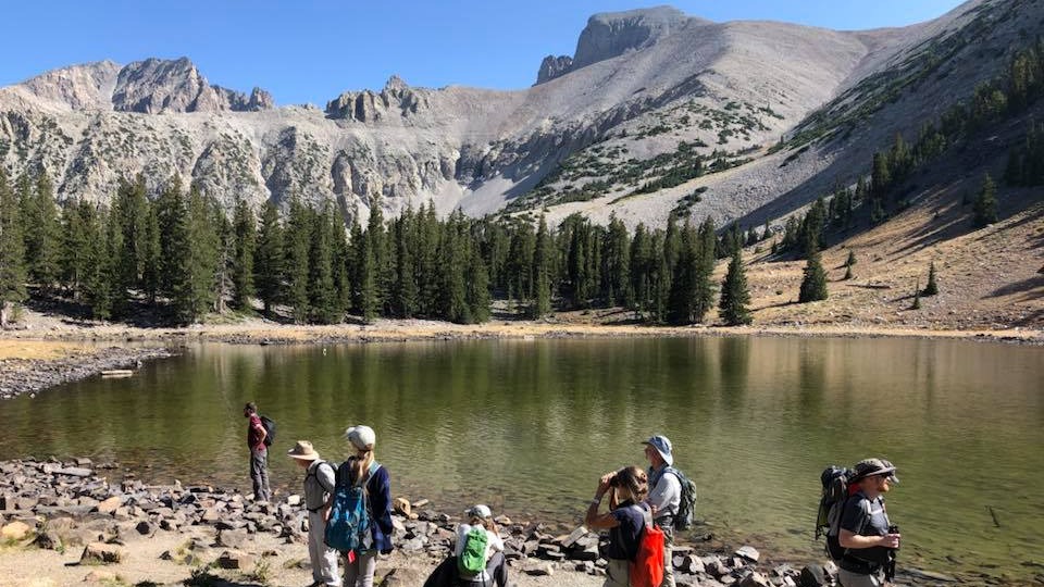 Group of people gathered around a mountain lake.